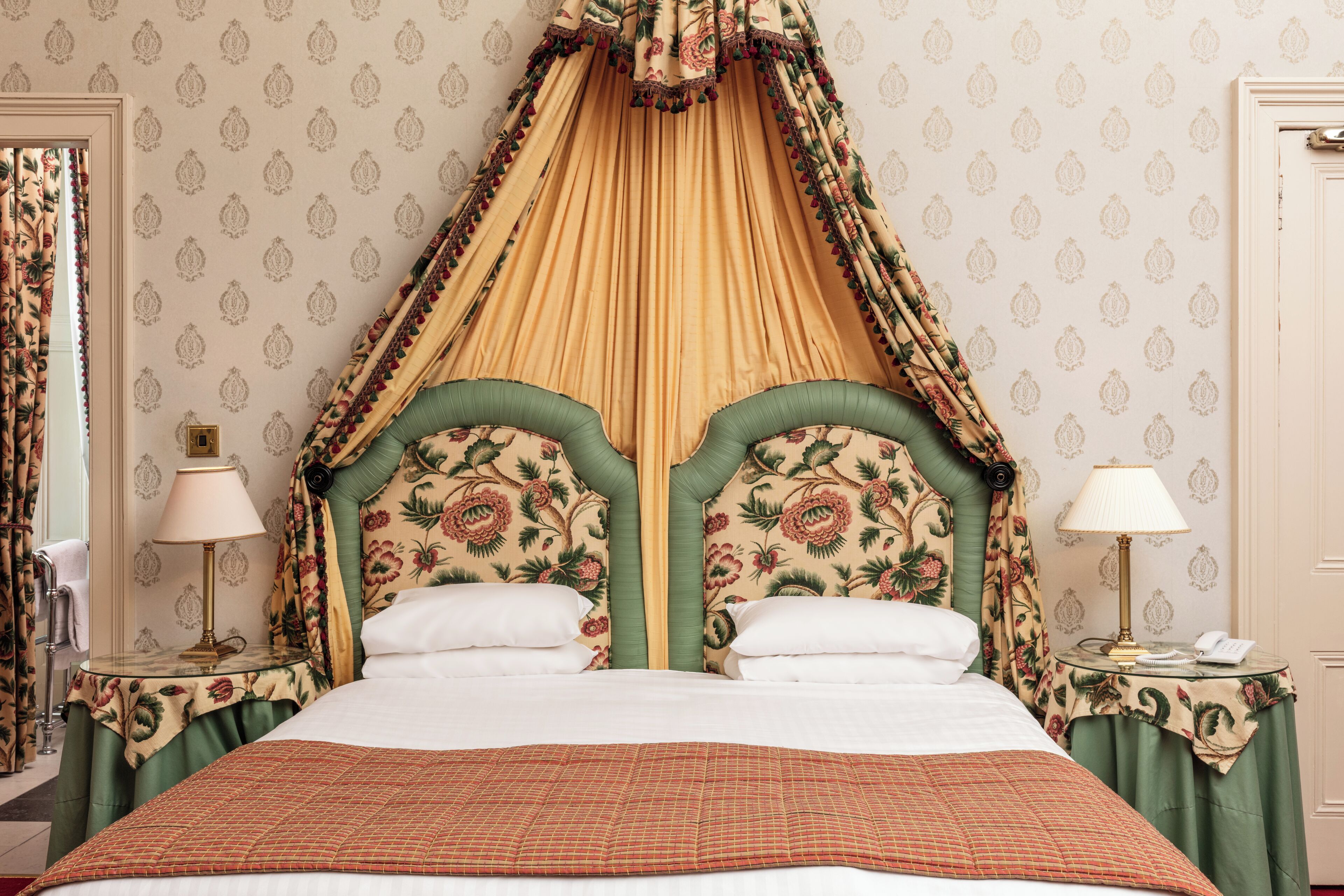 A bed with a canopy, green upholstered headboard, and floral-patterned curtains.