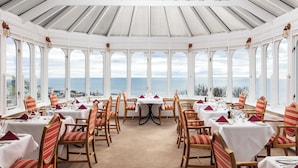 A restaurant with a view of the sea, featuring white tables and chairs, and a glass ceiling. - Fernhill Hotel (Stranraer)
