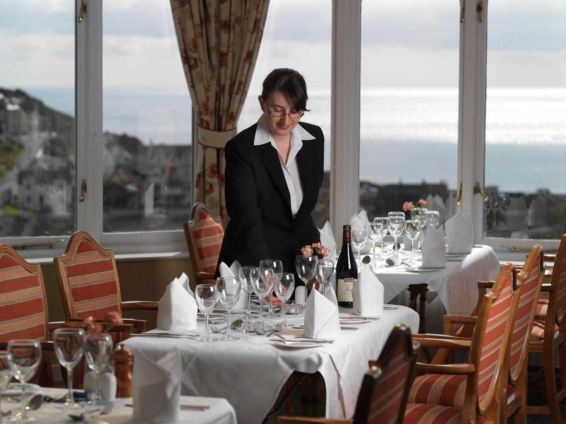 A dining area with a table set for a meal, chairs, and a view of the city through large windows.
