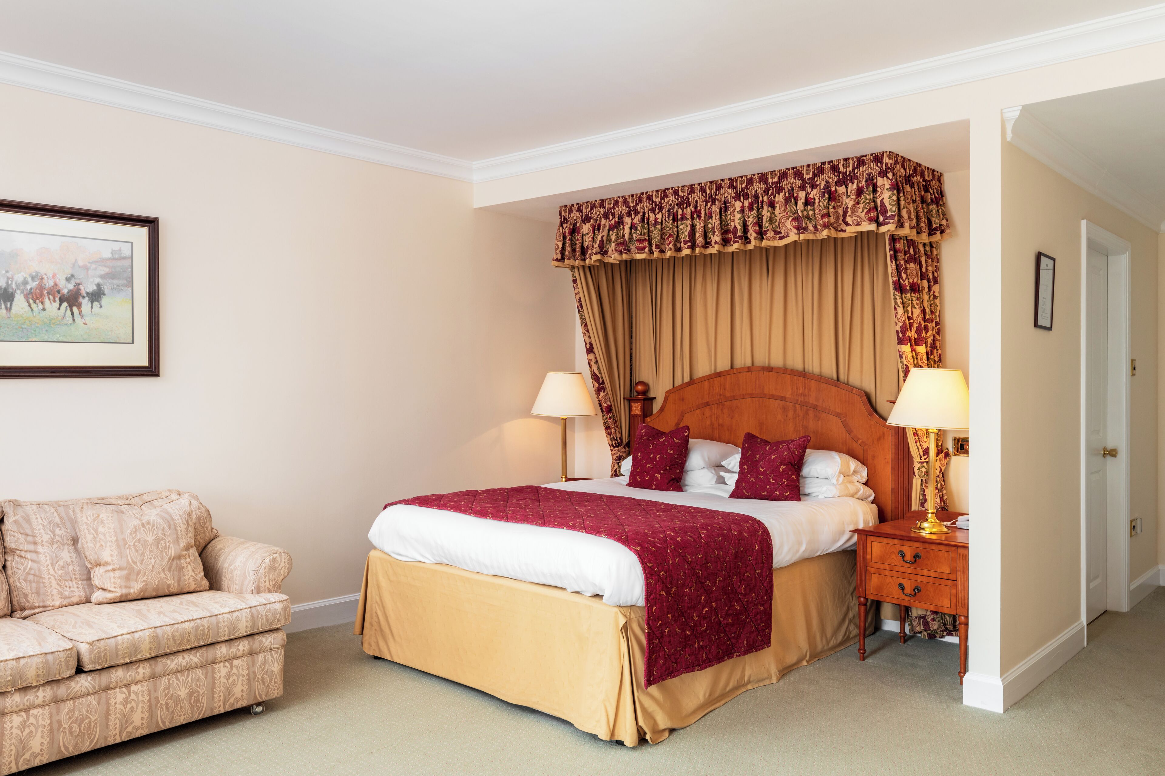 A neatly arranged hotel room with a large bed, a bedside table with lamps, a sofa, and a framed picture on the wall.