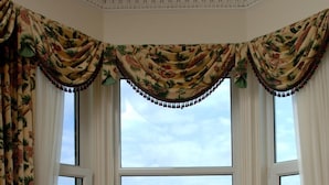 A room with a bay window overlooking a coastal town, a green sofa, a wooden table with a vase of flowers, and a book. - Fernhill Hotel (Stranraer)