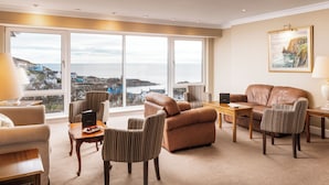 A spacious living room with a large window offering a view of the sea and buildings, a leather sofa, striped armchairs, and a wooden coffee table. - Fernhill Hotel (Stranraer)