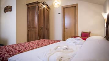 A hotel room with a bed, a wooden wardrobe, a red and white patterned bedspread, and a red chair.