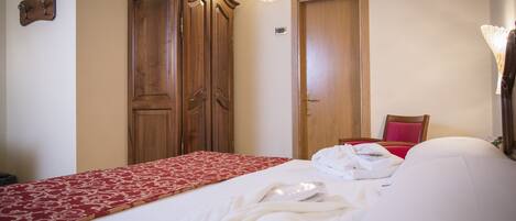 Habitación de hotel con cama, armario de madera, colcha de cama con estampado rojo y blanco, y una silla roja.