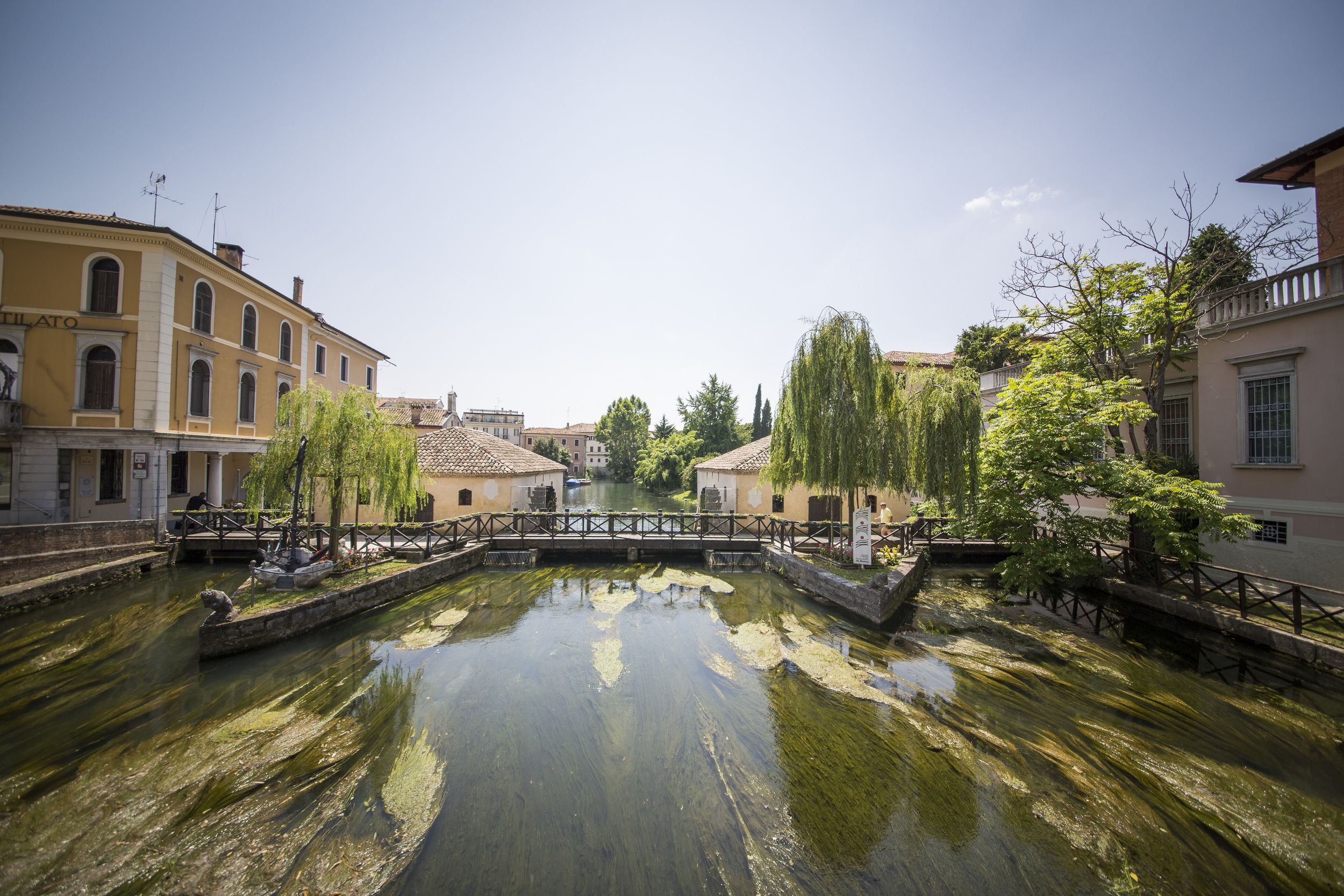 Ein Kanal mit einer Brücke, umgeben von historischen Gebäuden und Bäumen.