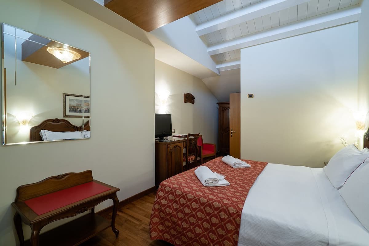 A hotel room with a bed, a desk, a chair, a television, and a mirror.
