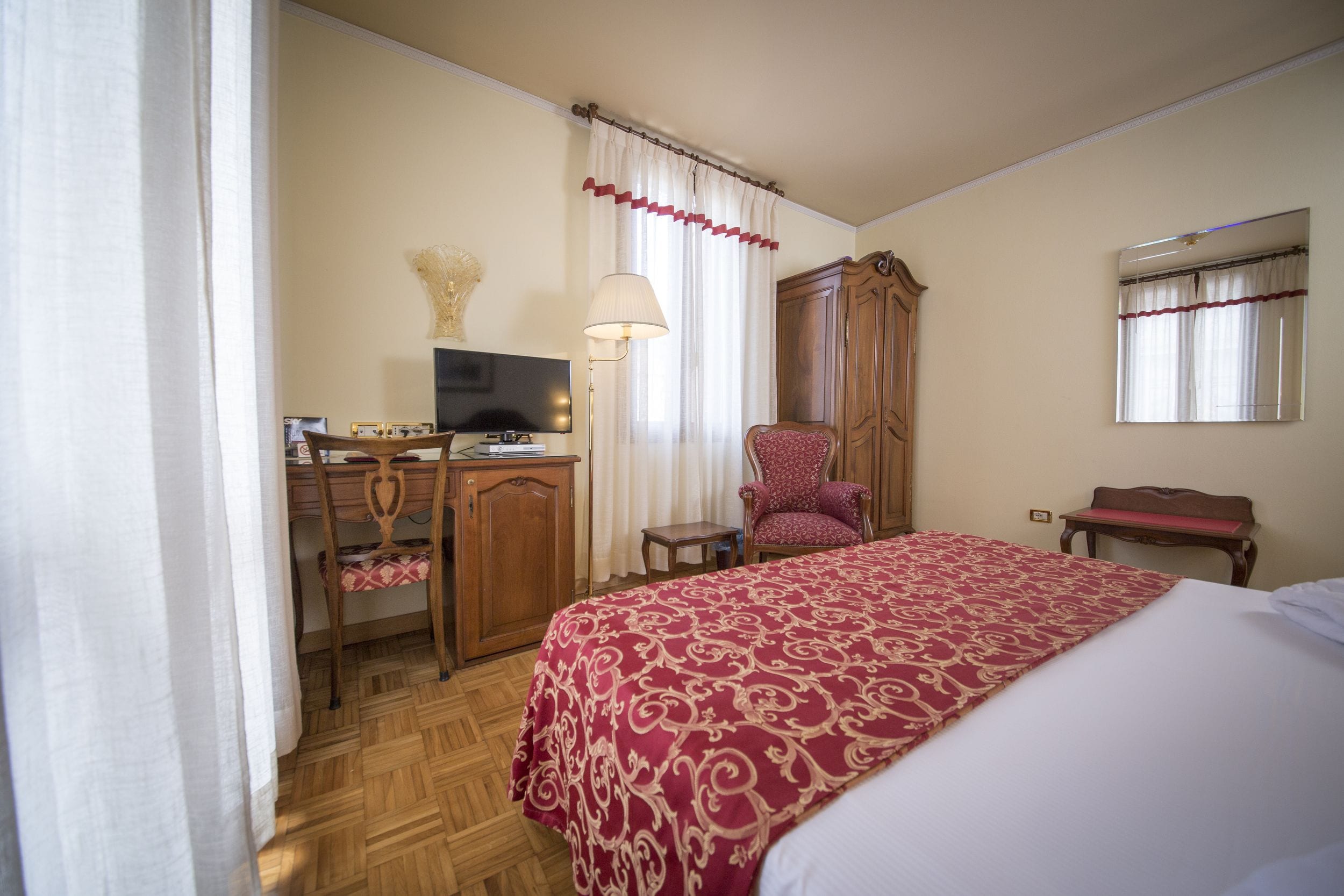 Una habitación de hotel con cama, escritorio, silla, armario y espejo.