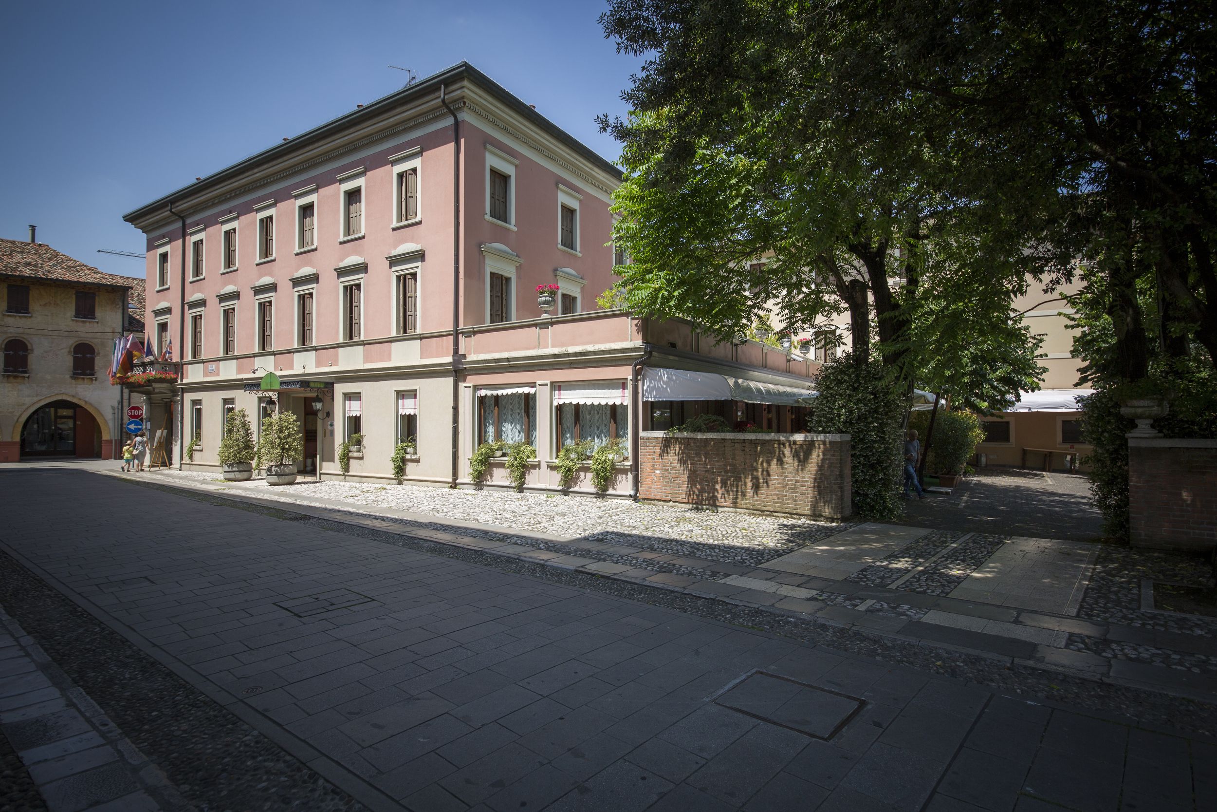 A building with a row of shops on the ground floor, a balcony with potted plants, and a clear sky.