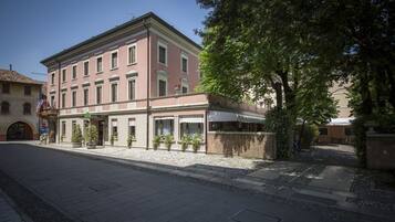 A building with a row of shops on the ground floor, a balcony with potted plants, and a clear sky.