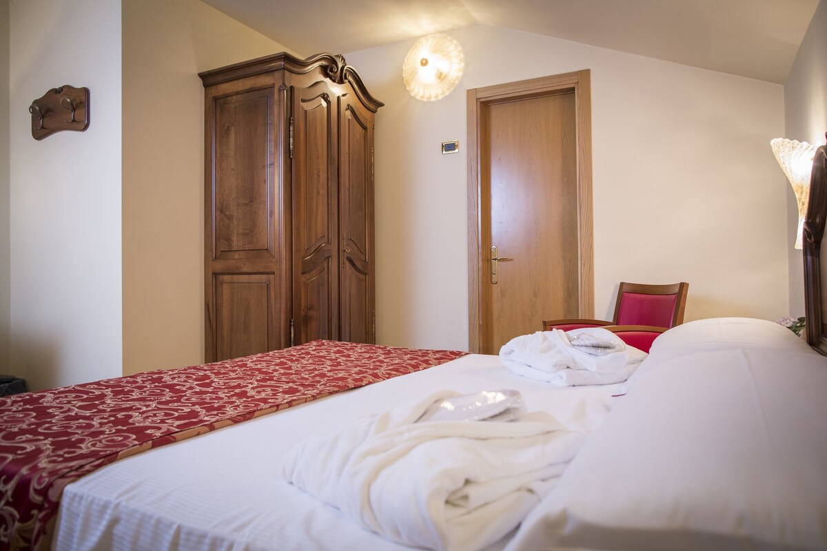 A hotel room with a bed, a wooden wardrobe, a red and white patterned bedspread, and a red chair.