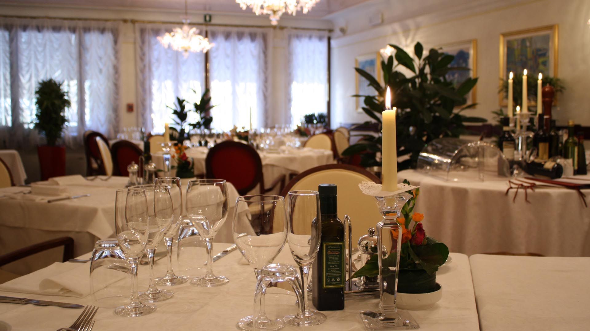 A dining area with tables set for a meal, featuring wine glasses, a bottle of wine, and a candle.