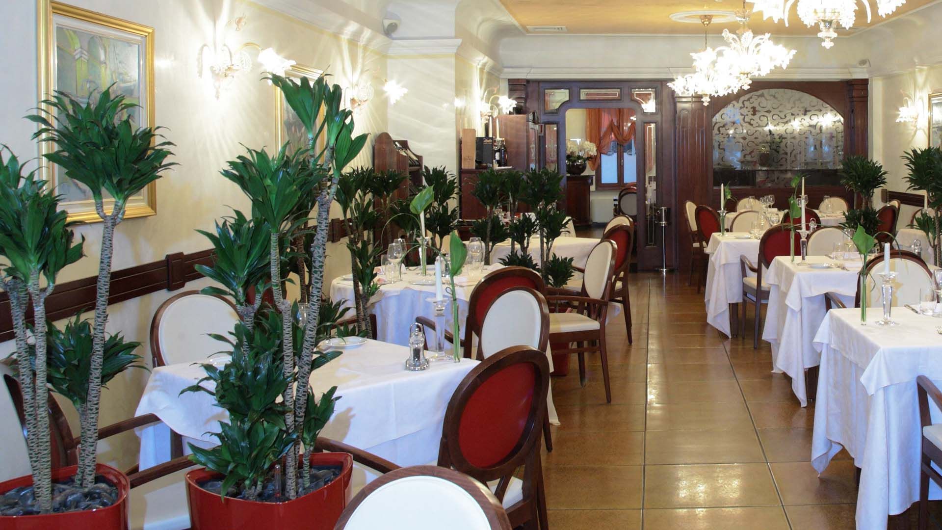 Un restaurante con mesas dispuestas para comer, plantas en macetas y candelabros.
