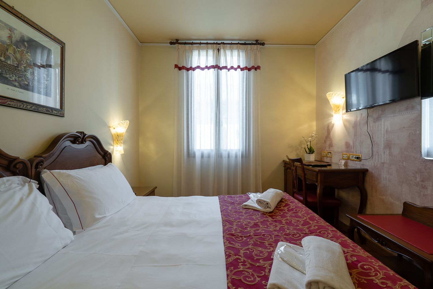 A hotel room with a bed, a desk, a chair, a TV, and a window with curtains.