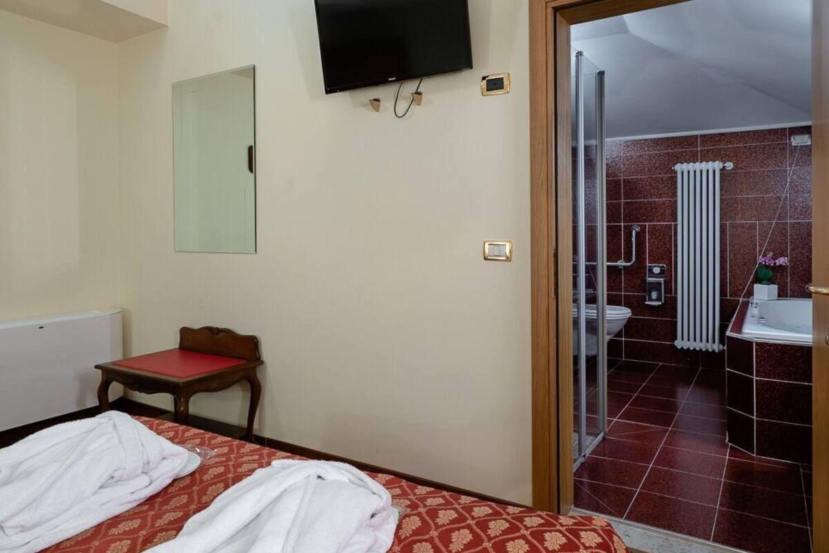 A hotel room with a bed, a television, a small table, and a bathroom visible through an open door.