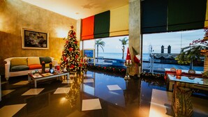A hotel lobby with a Christmas tree, a sofa, a coffee table, and a view of the sea through large windows. - Hotel Miramar (Arrecife)