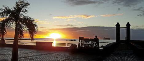 A sunset view at the Museo de Historia de Arrecife, with a palm tree and a ship in the background.