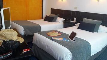 Una habitación de hotel con dos camas, un escritorio con una laptop, una cámara y un sombrero.