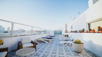 Una terraza en la azotea con sillones, una mesa, plantas en macetas y vistas a la ciudad.