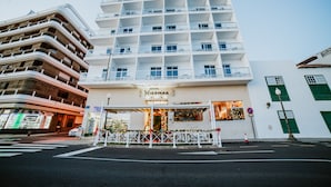 A multi-story hotel with a modern architectural design, featuring balconies on each floor and a ground-level entrance with a Christmas display. - Hotel Miramar (Arrecife)