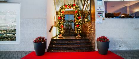 Entrada de hotel con alfombra roja, un adorno navideño y dos macetas.