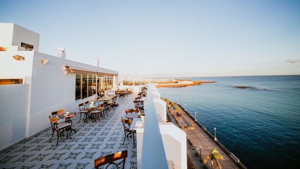 A rooftop terrace with tables and chairs overlooking a coastal area. - Hotel Miramar (Arrecife)