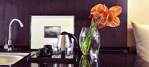 A modern kitchen with a black countertop, a stainless steel kettle, a coffee maker, and a vase with flowers. - Langkawi Lagoon Resort (Langkawi)