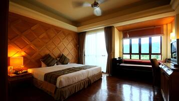 A hotel room with a large bed, a desk with a computer, a window with a view, and a ceiling fan.