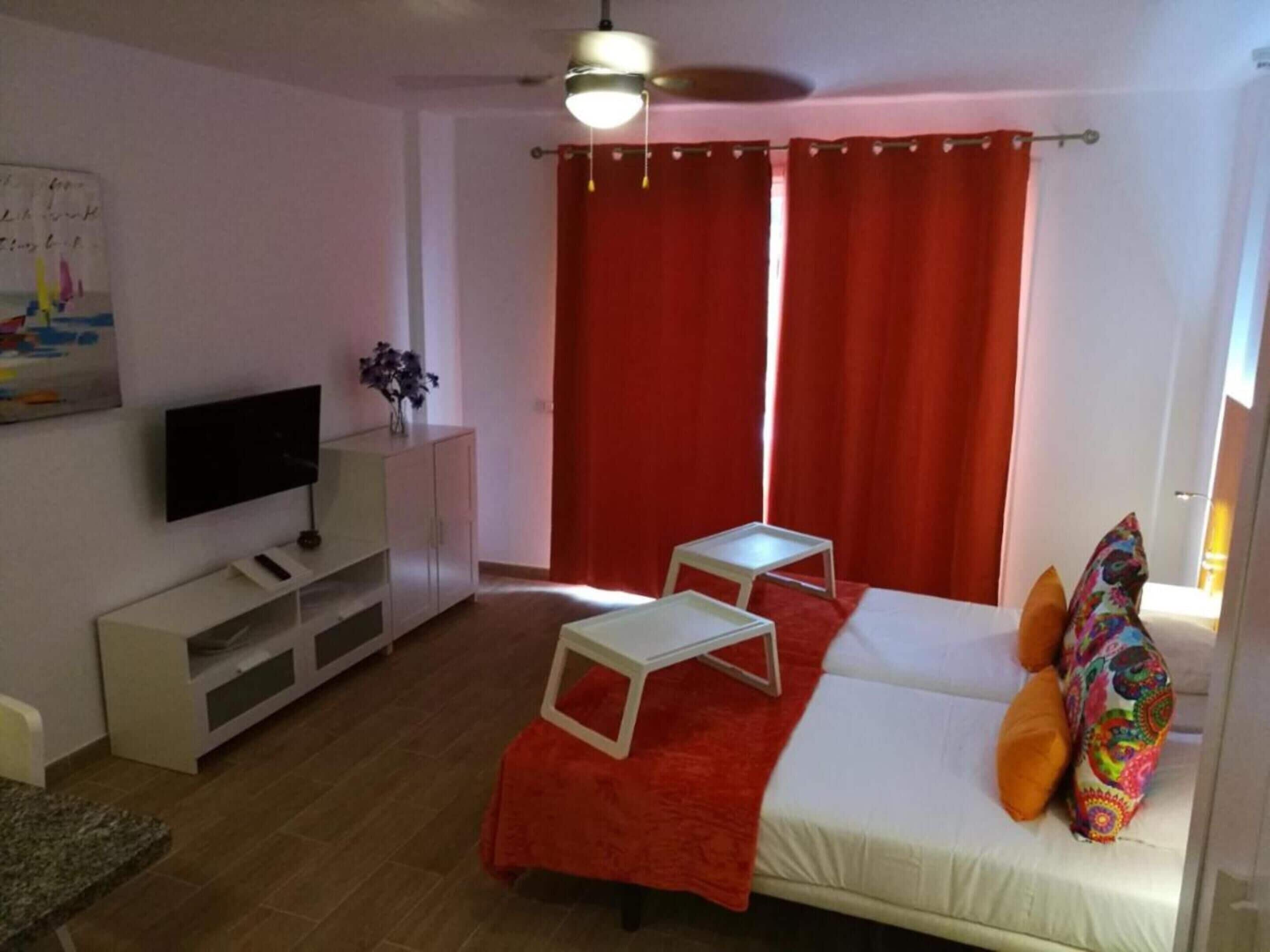 Un soggiorno moderno con un divano, una TV, un tavolino e una tenda rossa.