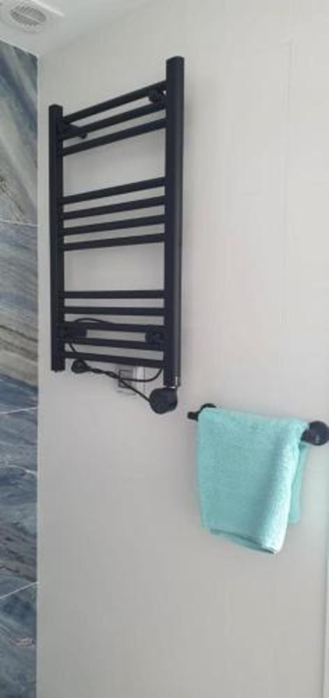 Un perchero negro con una toalla azul claro colgada, fijado a una pared blanca.