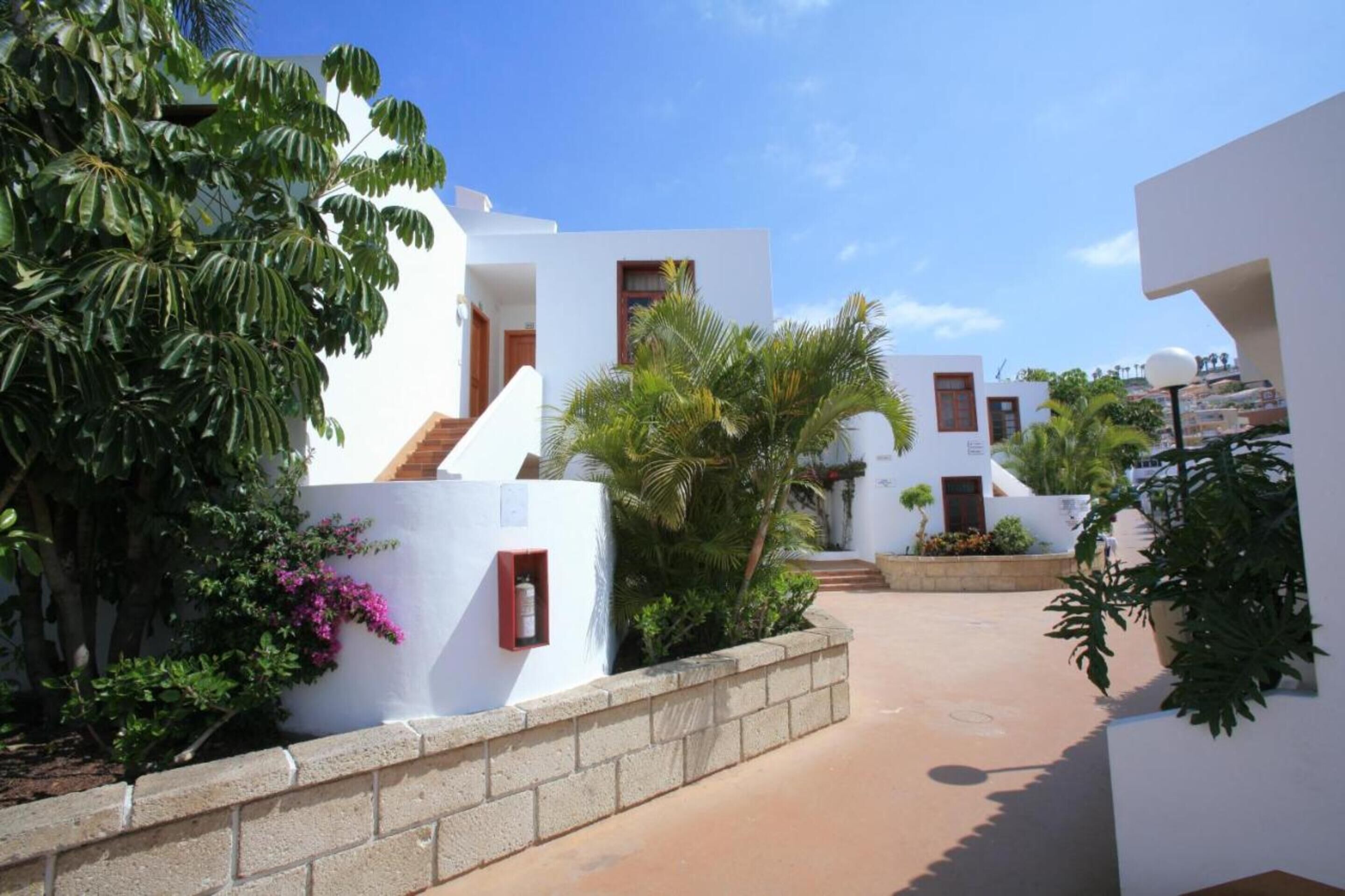 Una villa moderna con paredes blancas, un patio empedrado y plantas tropicales.