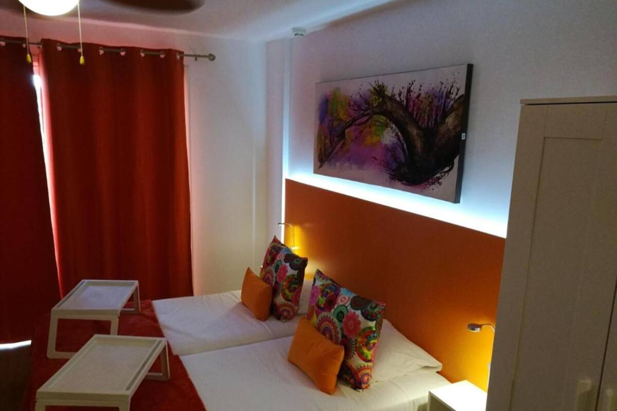 Une chambre d’hôtel avec deux lits, un rideau rouge, un tableau au mur et une porte blanche.