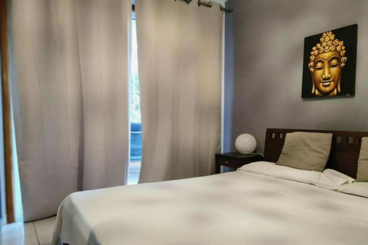 Une chambre d’hôtel avec un lit, des rideaux, une statue de Bouddha fixée au mur et une table de chevet avec une lampe.