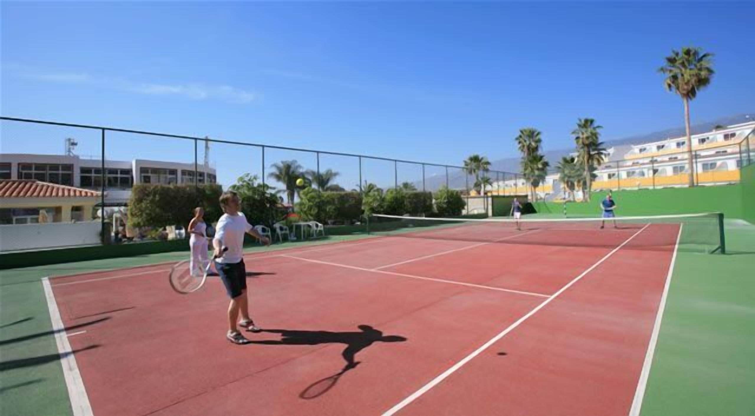 Un court de tennis extérieur avec deux joueurs, un filet et une clôture.