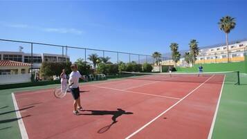 Un court de tennis extérieur avec deux joueurs, un filet et une clôture.