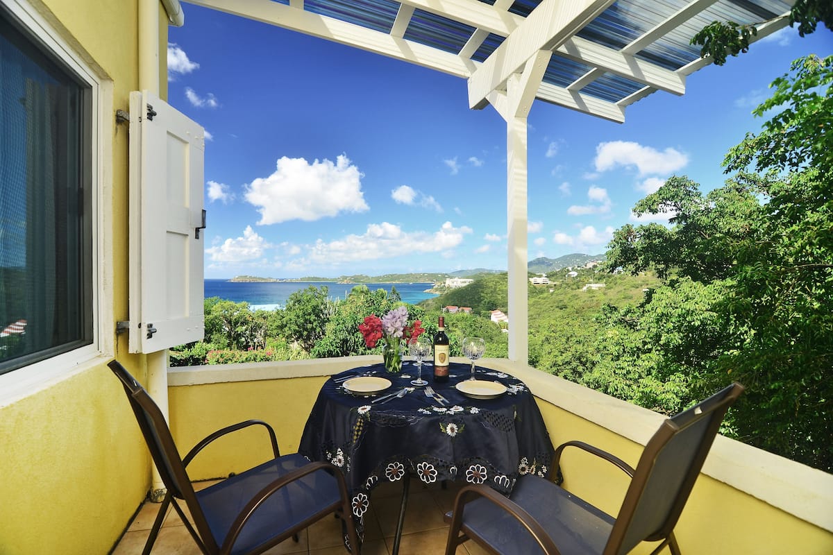 A balcony with a table set for two, overlooking a scenic view of the sea and greenery.