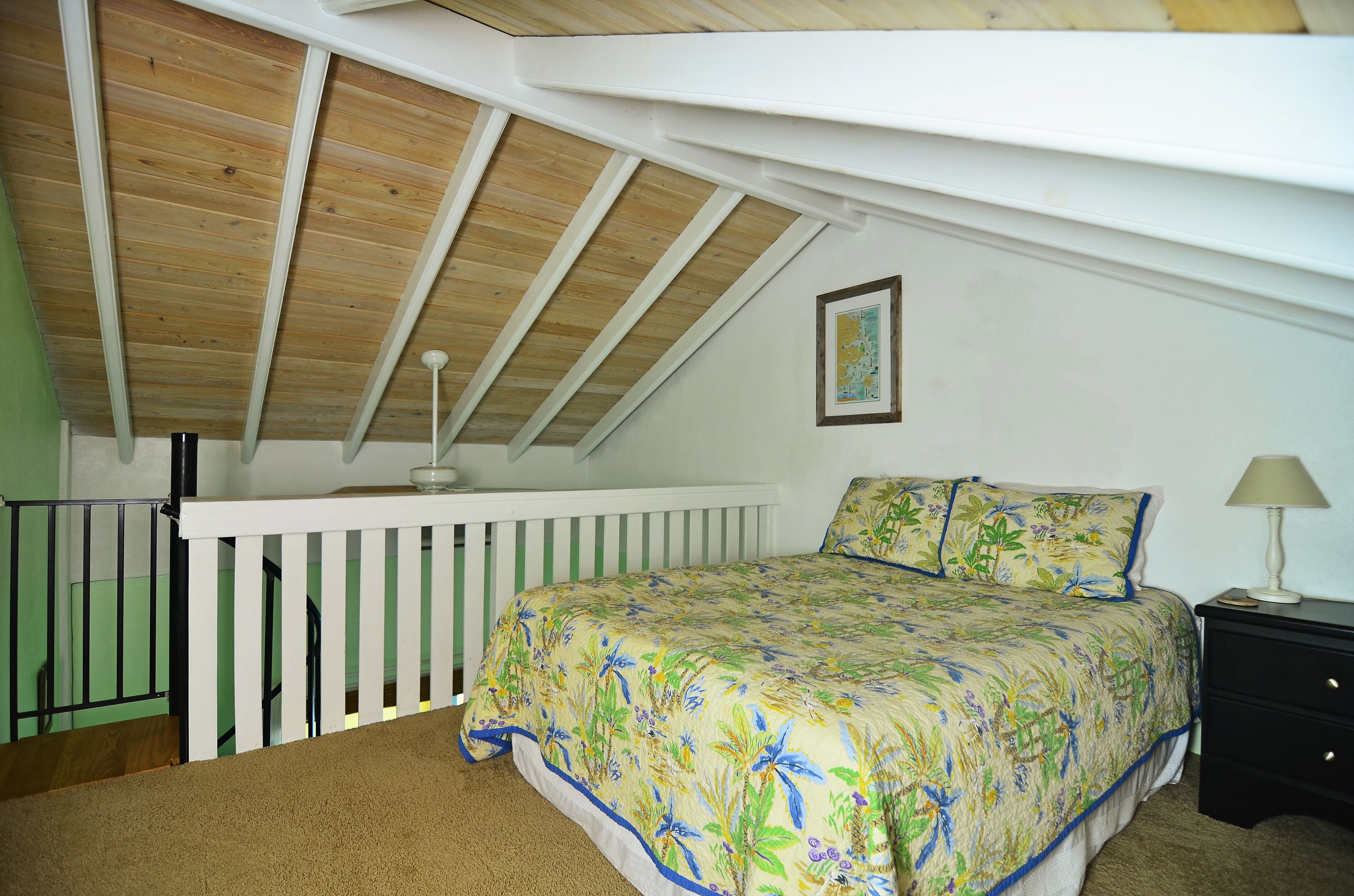 Een slaapkamer met schuine balken, een bed met bloemenbeddengoed, een nachtkastje en een lijst met een foto aan de muur.
