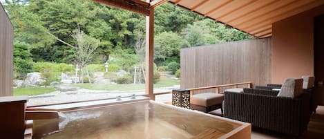 A hot spring bath area with a wooden deck, seating, and a view of a forested landscape.