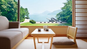 Una habitación con un sofá, una mesa con tetera y tazas, y vistas a un parque y una masa de agua.