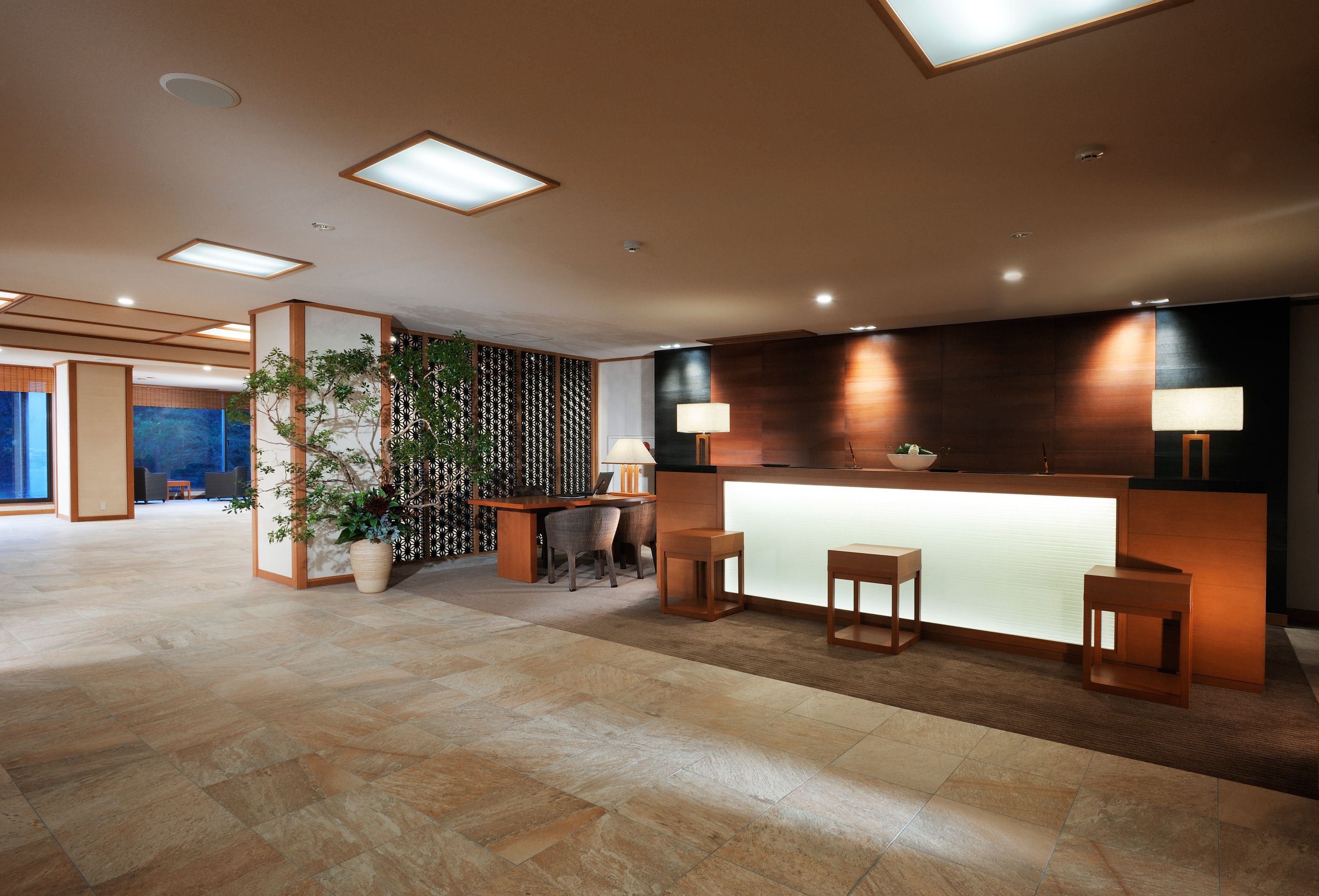 A modern reception area with a wooden reception desk, two stools, and a potted plant.
