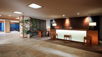A modern reception area with a wooden reception desk, two stools, and a potted plant.