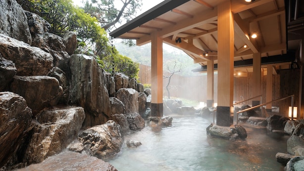 Un onsen japonés tradicional con estructura de madera, terreno rocoso y un manantial termal que fluye.