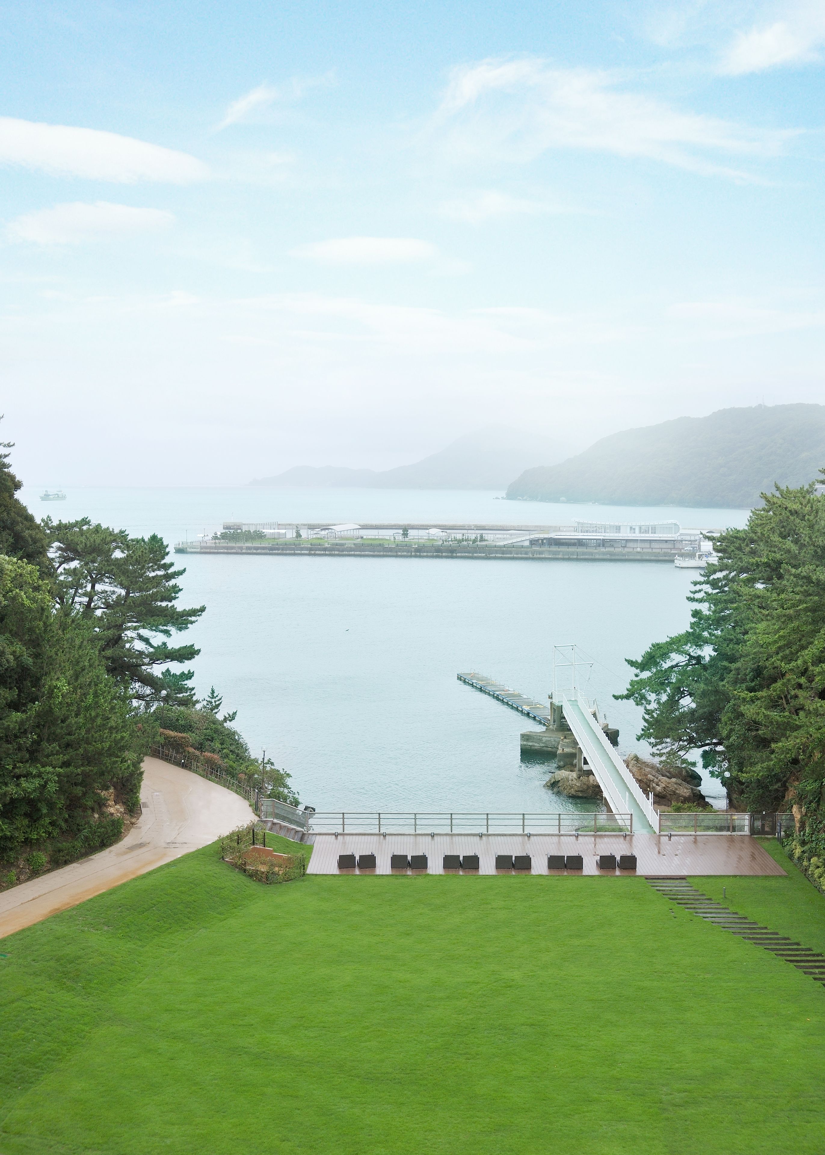 A coastal view with a grassy area, a bridge, and a distant peninsula.