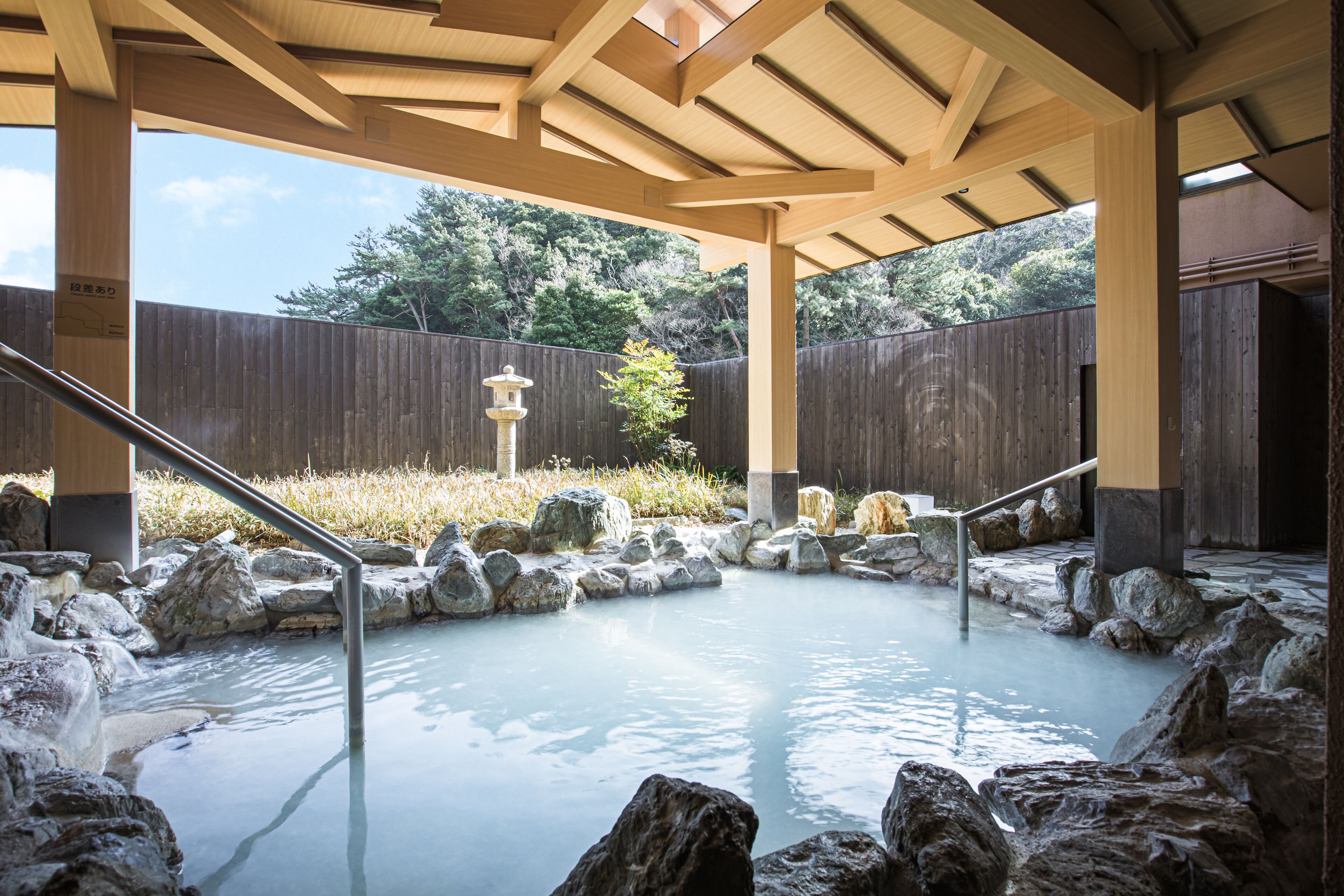A hot spring area with a wooden deck, stone rocks, and a wooden fence in the background.