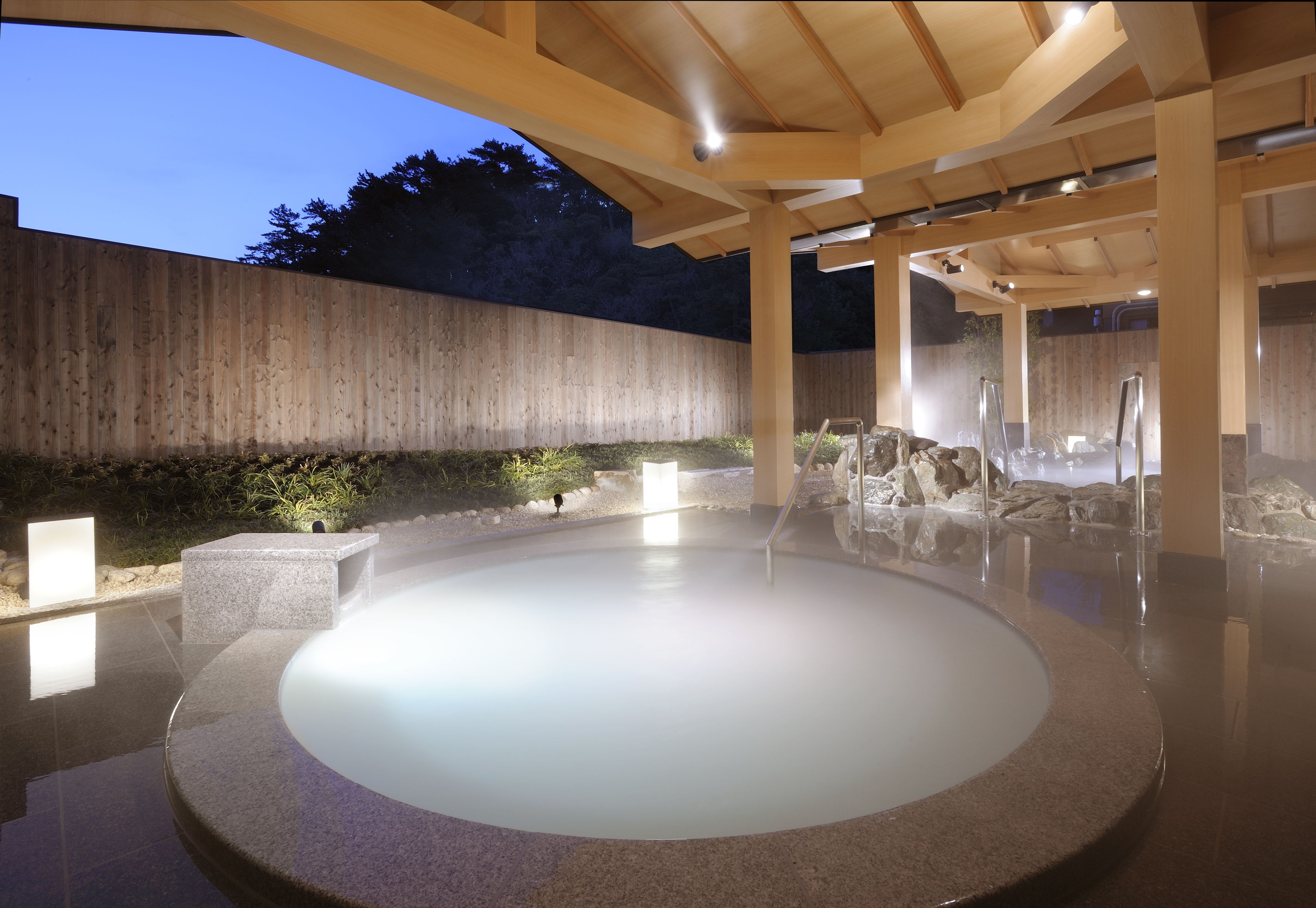 Un área de aguas termales con una pérgola de madera, asientos de piedra y un muro de piedra.