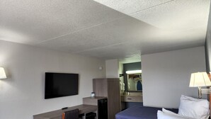 A hotel room with two beds, a desk, a TV, a mirror, and a lamp.