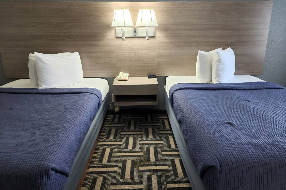 A hotel room with two beds, a headboard with wall-mounted lamps, a bedside phone, and a patterned carpet.