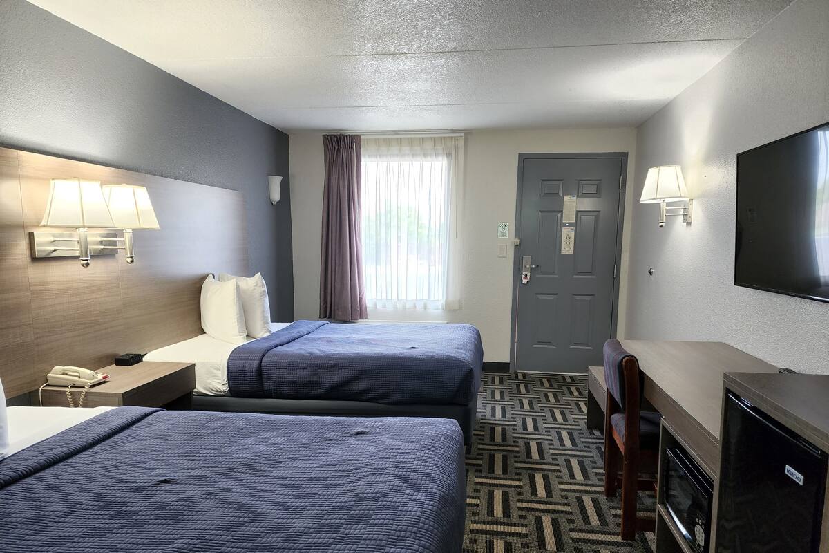 A hotel room with two beds, a desk, a TV, and a window with curtains.