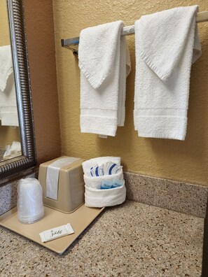 A bathroom with two white towels hanging on a metal rack, a hand dryer, a tissue dispenser, and a small trash bin.