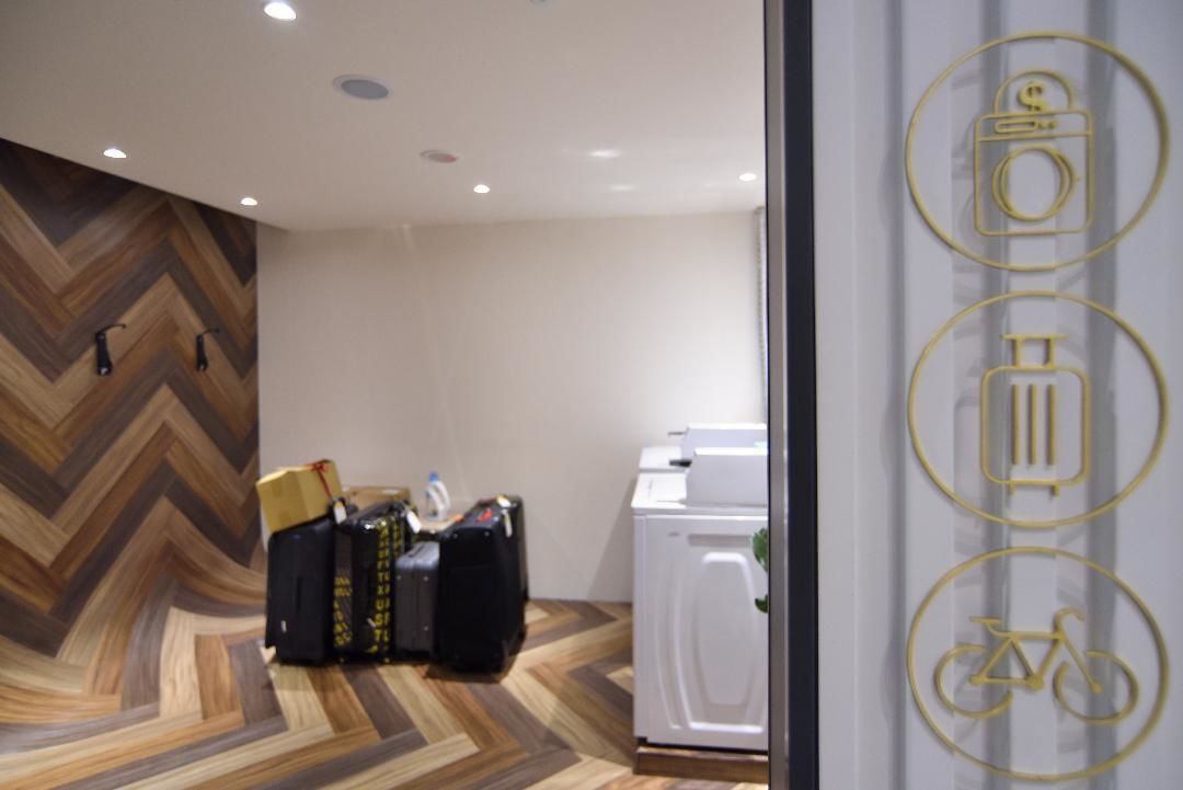 A hotel room with a herringbone-patterned floor, a washing machine, and a wall with three icons indicating amenities.