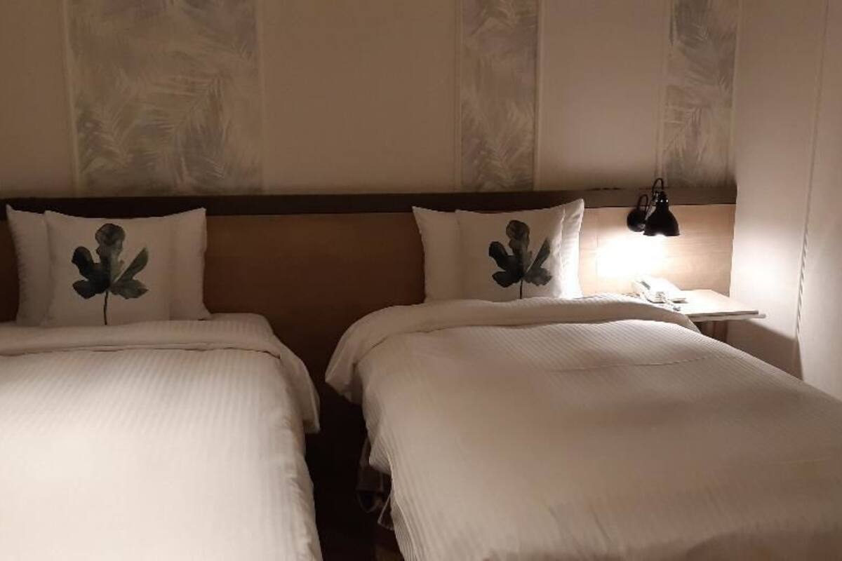 Une chambre d’hôtel avec deux lits, une table de chevet et une fenêtre avec des stores.